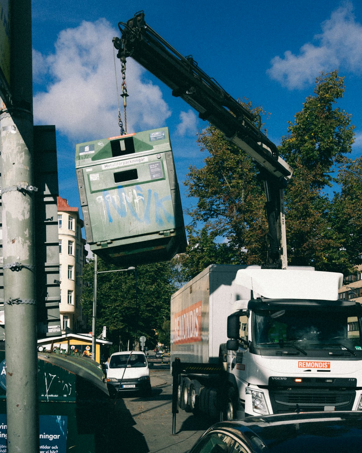 Een vuilniswagen tilt een groene container op in de stad.